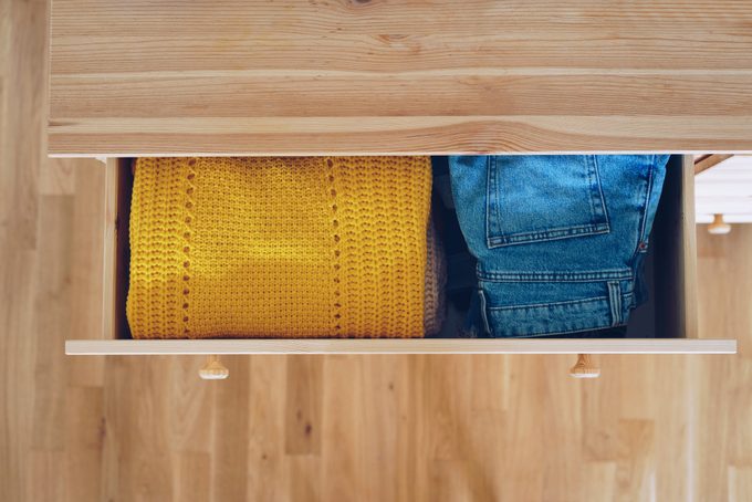 overhead view of neatly folded clothes, yellow sweater next to jeans, in an open drawer