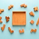 pieces of a wooden iq puzzle scattered around the puzzle frame. blue background