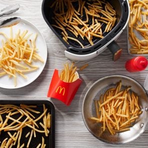 reheated mcdonalds fries on a plate, toaster oven pan, baking sheet, air fryer basket, and pan on light gray wood background