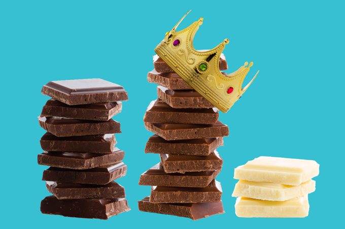 stack of dark chocolate, milk chocolate, and white chocolate on a blue background. the milk chocolate has a crown on top; the white chocolate stack is the shortest